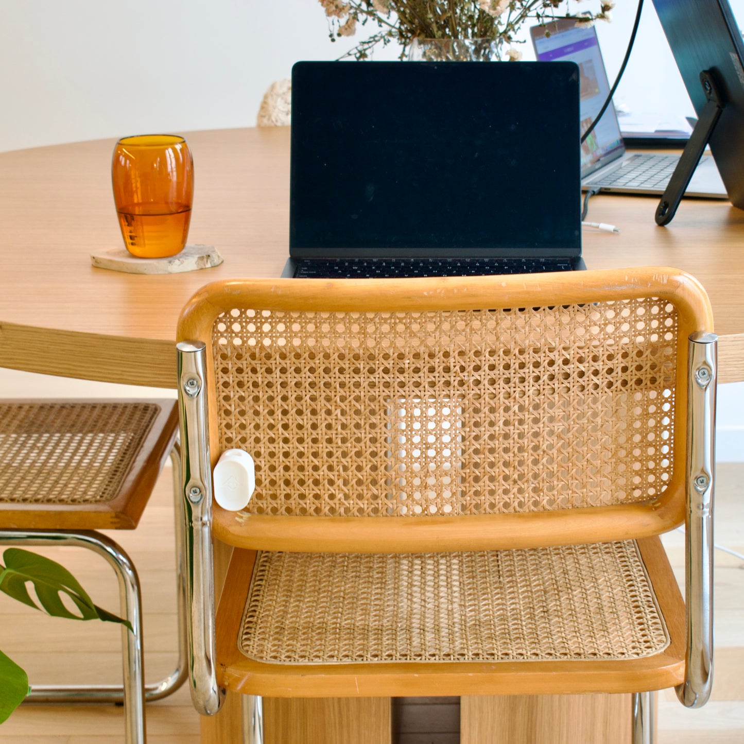 Wooden chair with wicker backrest in front of a desk with a laptop and a glass.