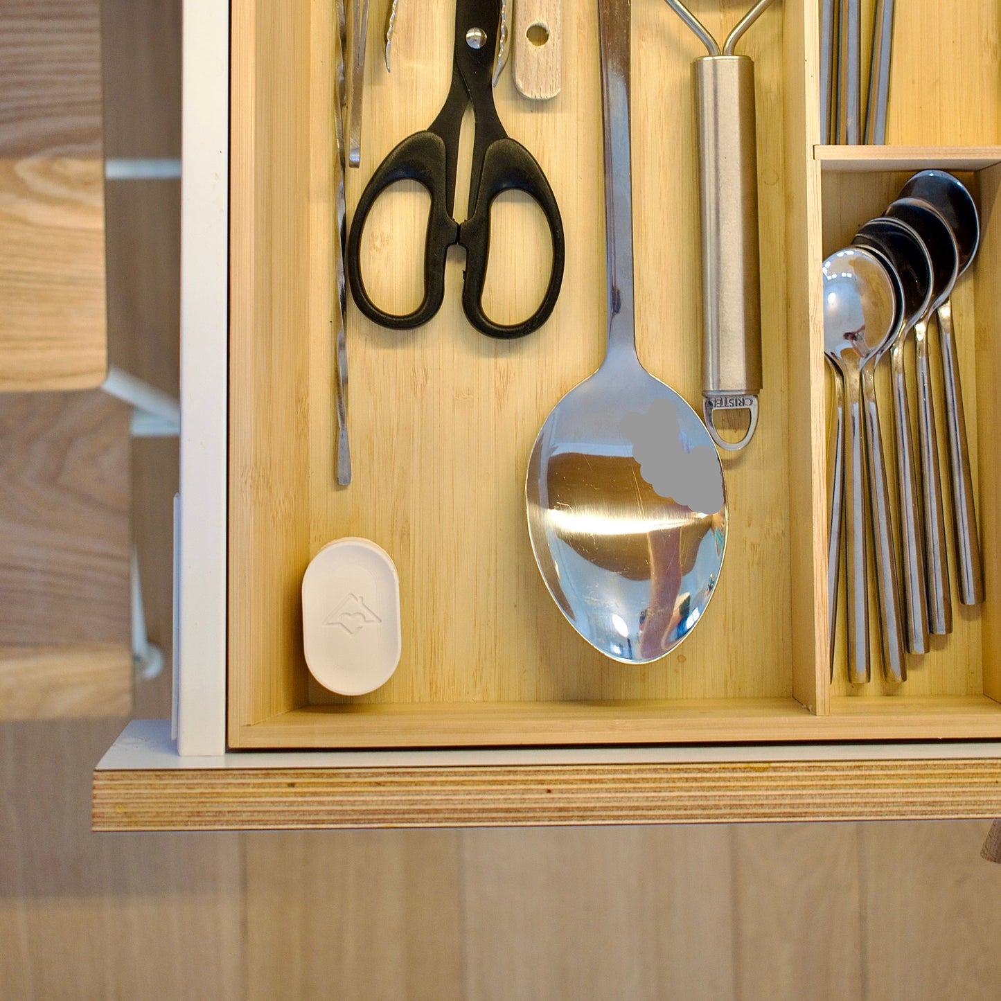 Wooden cutlery organizer with silverware including a spoon, scissors, and other utensils.