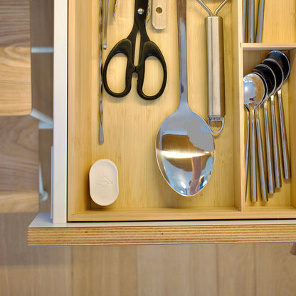 Wooden cutlery organizer with silverware including a spoon, scissors, and other utensils.