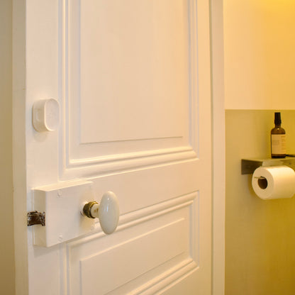 Close-up of a white door with a doorknob and a roll of toilet paper on a wall.